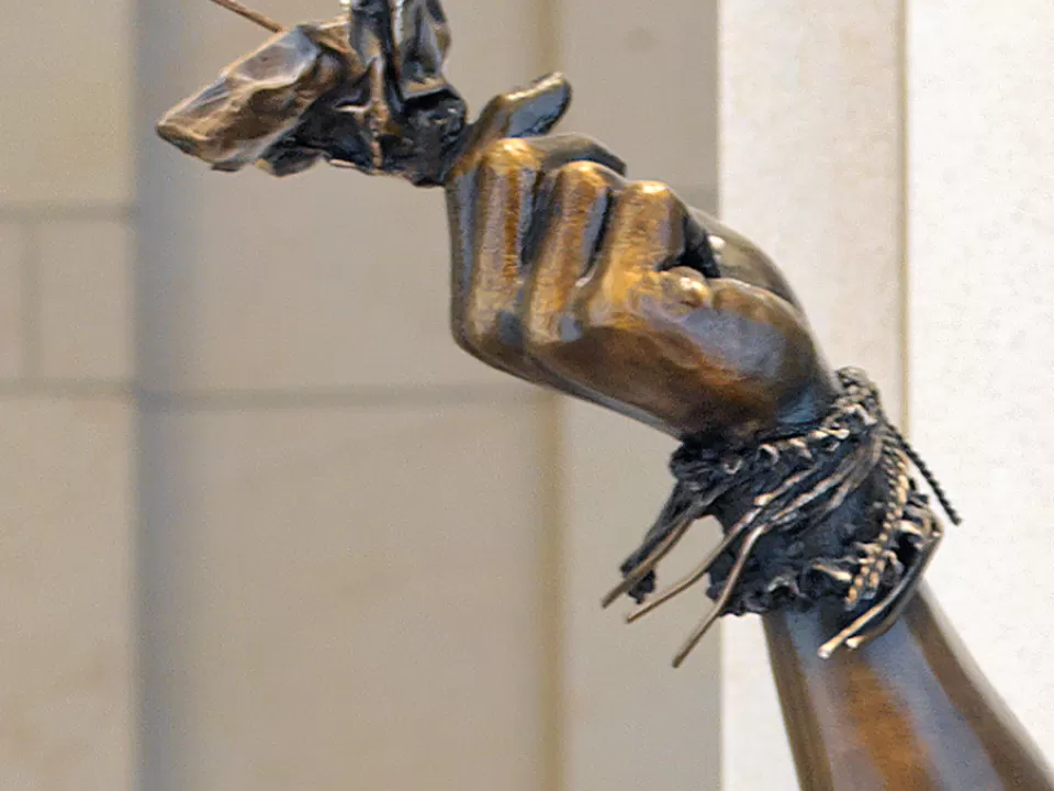 Sculpture detail of a person's hand and arm.