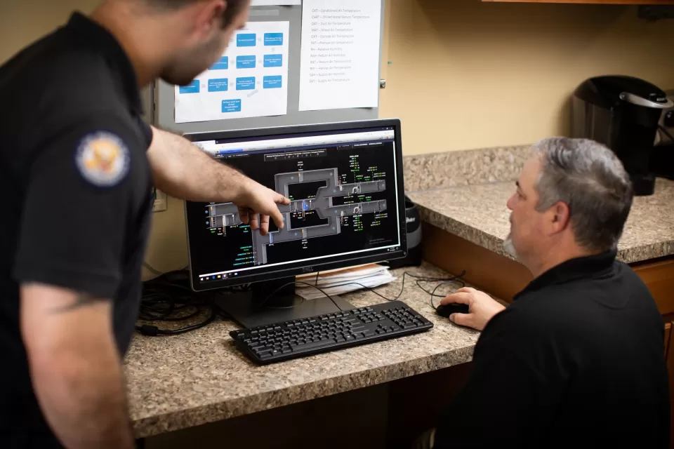 Electronics Technician Edward Williams and A/C Equipment Mechanic Justin Zibragos discuss an air handling unit’s operations using the AOC's Building Automation System graphics platform.