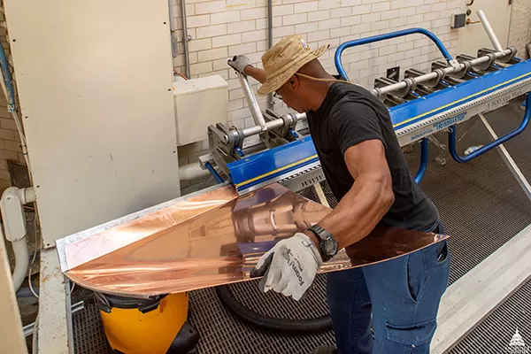 An AOC Sheet Metal Mechanic bends a copper wall flashing.