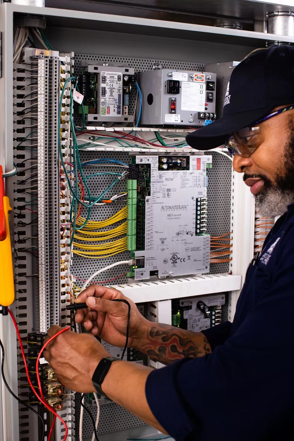 A/C Equipment Mechanic Horatio Evans tests for signal across two wires with a digital multimeter while troubleshooting air handling unit controls.