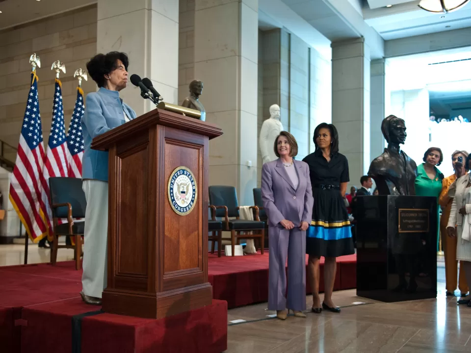 Person standing at podium with flags behind.