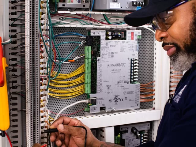A/C Equipment Mechanic Horatio Evans tests for signal across two wires with a digital multimeter while troubleshooting air handling unit controls.